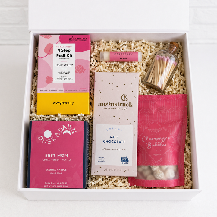 Gift box with various items including a pedicure kit, chocolate, and candles on a light background