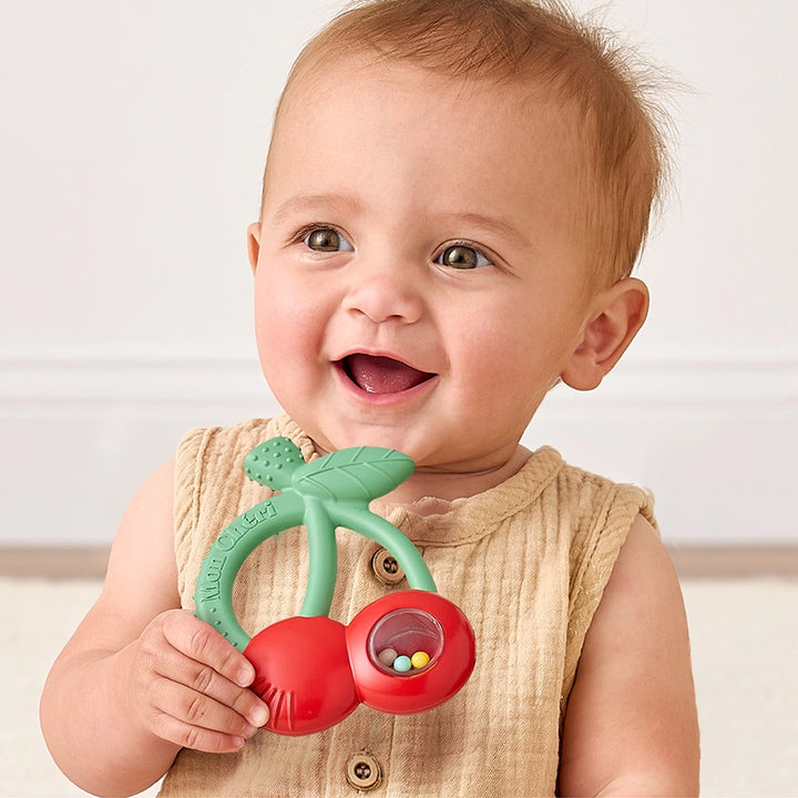 Smiling baby holding cherry-shaped silicone teether with rattle beads