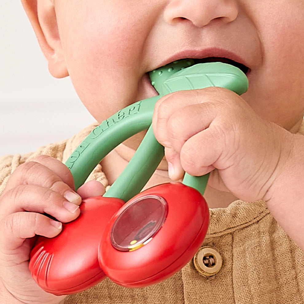 Baby holding and chewing on cherry-shaped silicone teether with green stem