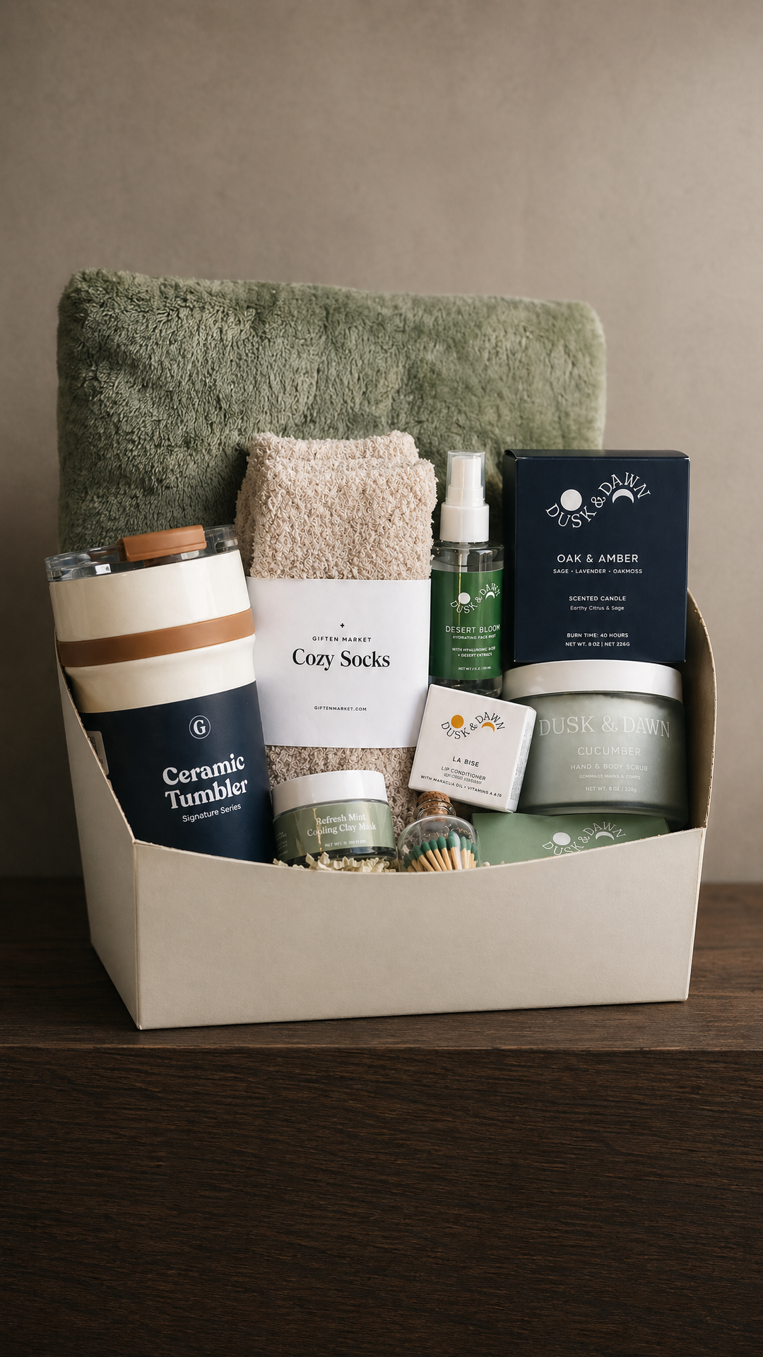 Gift box with green blanket, ceramic tumbler, cozy socks, candle, matches, and spa essentials