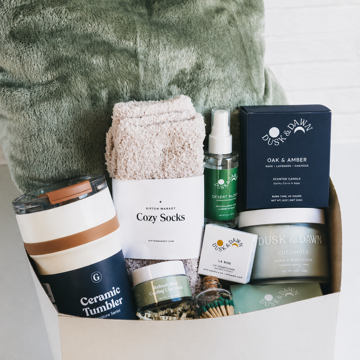 Gift box with cozy socks, ceramic tumbler, candle, body scrub, spray, and green blanket