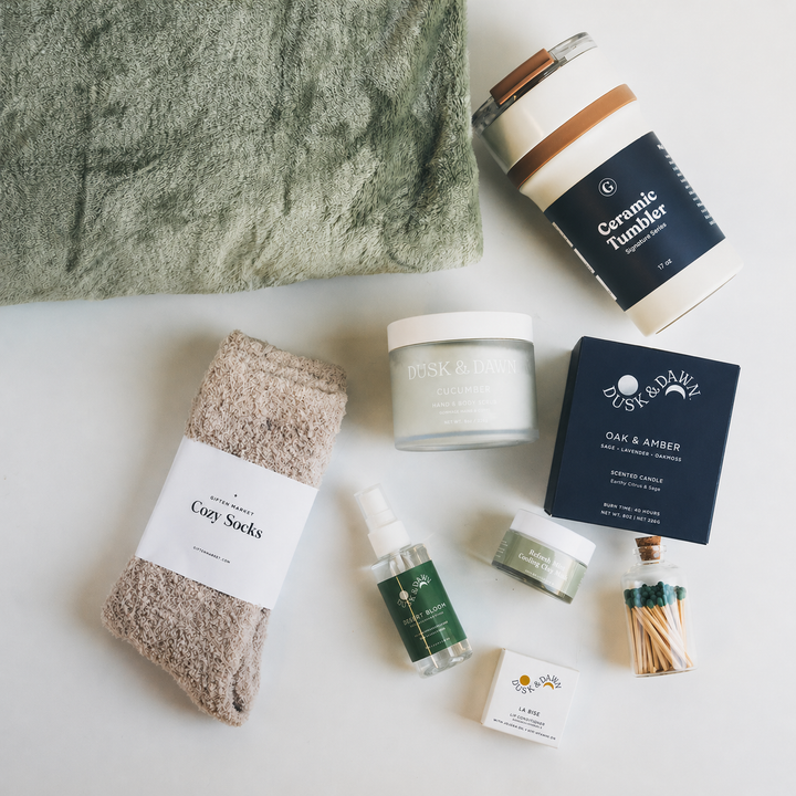 Sage green throw blanket, ceramic tumbler, cozy socks, candle, hand cream, and matches gift set