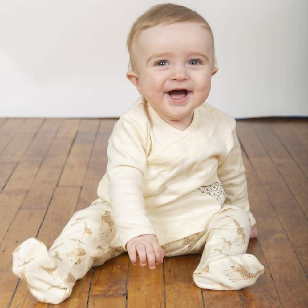 Smiling baby wearing cream footed pajamas with giraffe print on wood floor