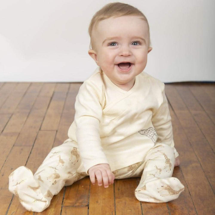 Smiling baby wearing cream footed pajamas with giraffe print on wood floor