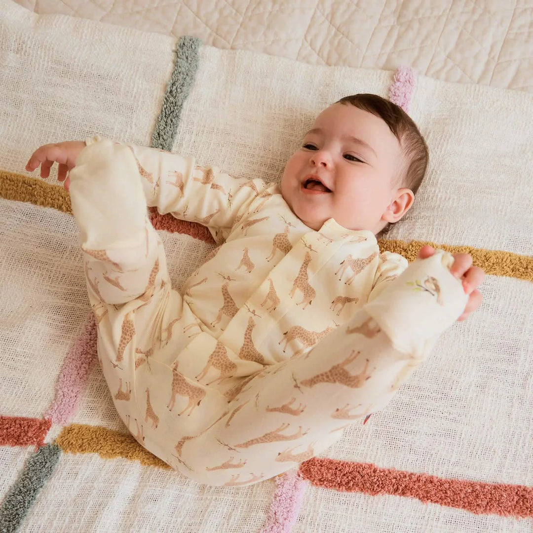 Baby wearing cream giraffe print footie pajamas on a soft textured blanket