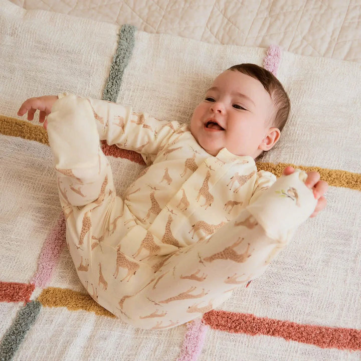 Baby wearing cream giraffe print footie pajamas on a soft textured blanket