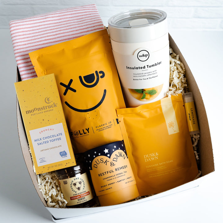Assorted products including a smiley face package, a tumbler, and snacks in a box on a light gray background