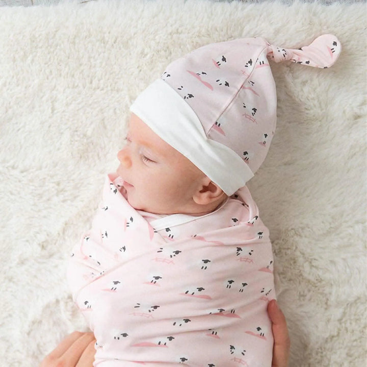 Newborn wrapped in a pink baby blanket and matching hat with sheep print on soft fabric