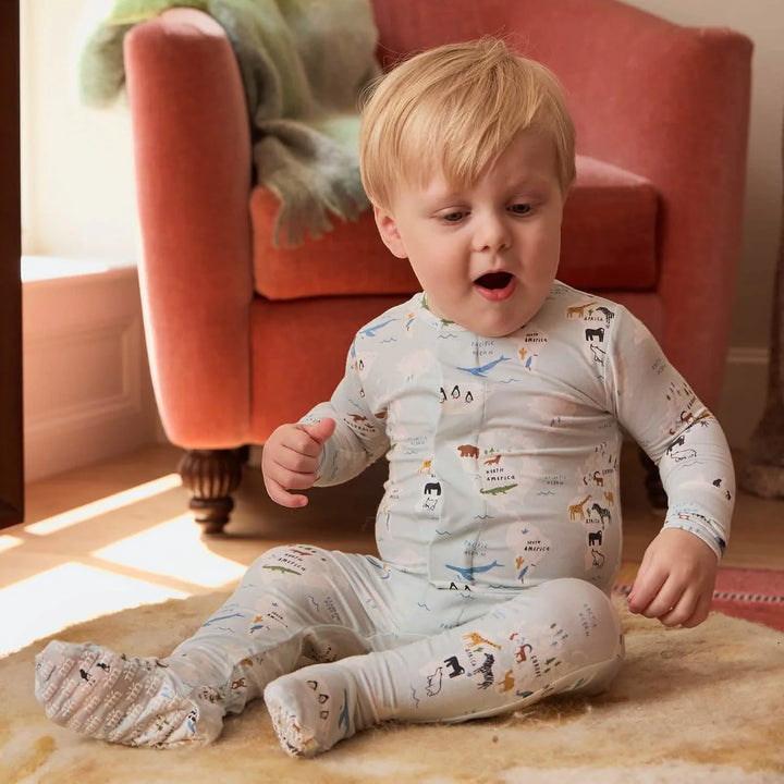 Baby wearing printed footie pajamas with animal designs, seated on a cozy rug