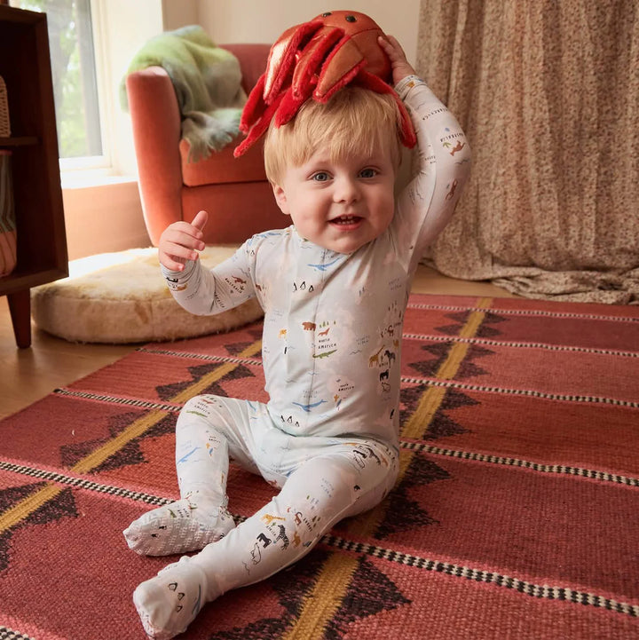 Baby in patterned footie pajamas sitting on rug, holding plush crab toy on head