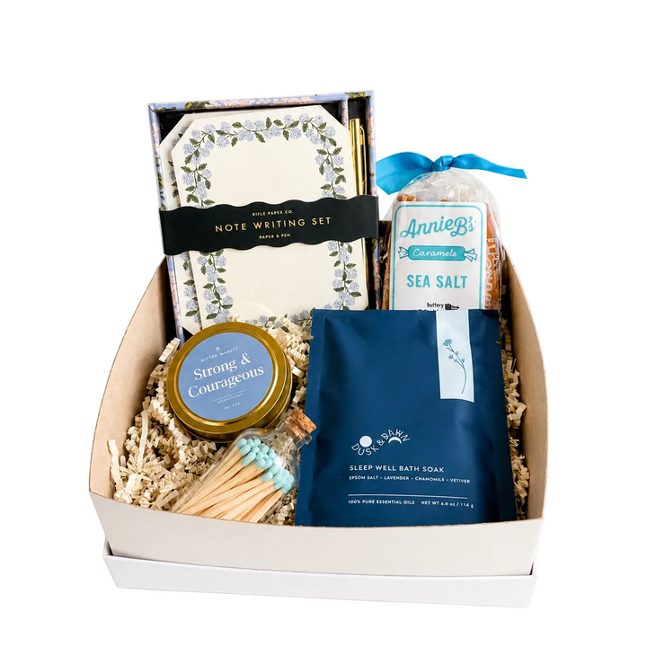 Gift box with stationery items, candles, and bath salts on a white background