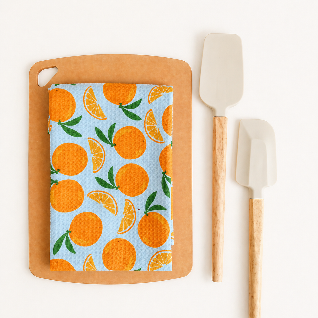 Wooden cutting board with a towel featuring orange pattern, accompanied by white spatulas on a white background.