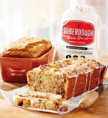 Apple fritter bread loaf with icing, ceramic baking dish, and bread mix packaging on table