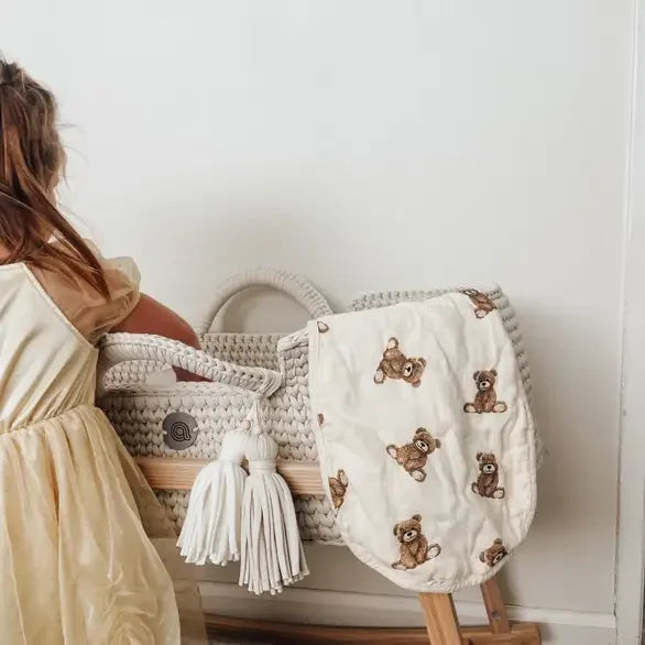 Bamboo muslin burp cloth with teddy bear print draped over woven bassinet