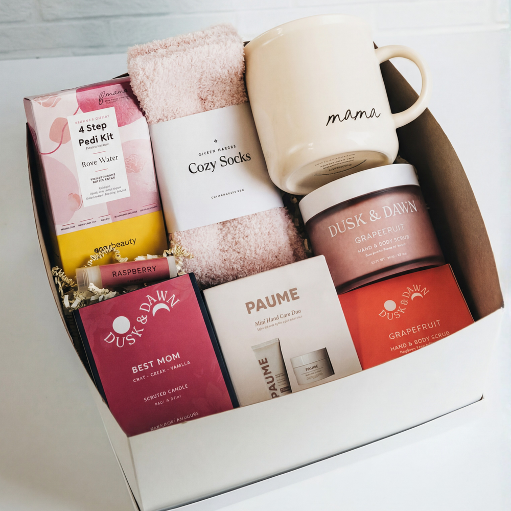 White gift box with cozy socks, candle, mug, body scrub, snacks, and hand care set