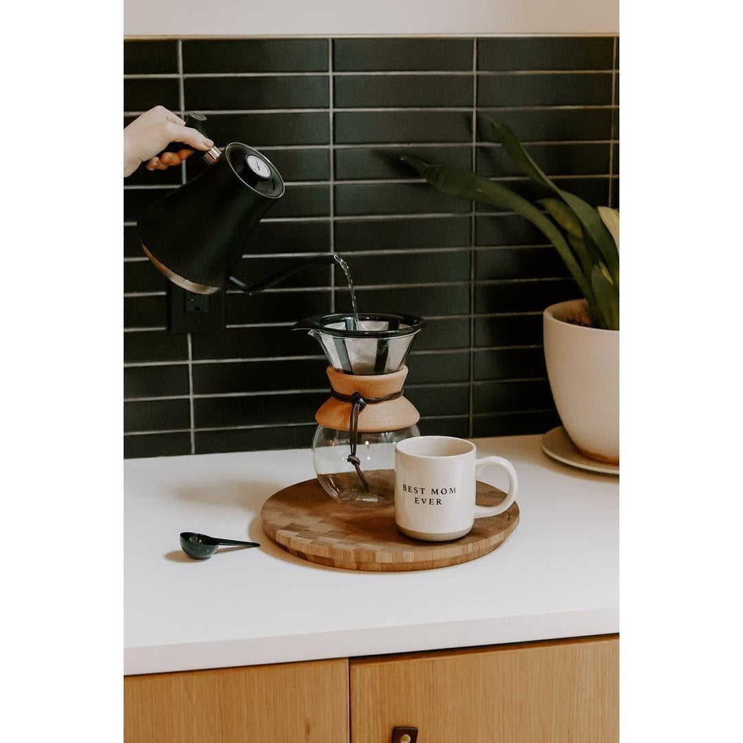 Stoneware coffee mug with 'Best Mom Ever' text beside pour-over set on kitchen counter