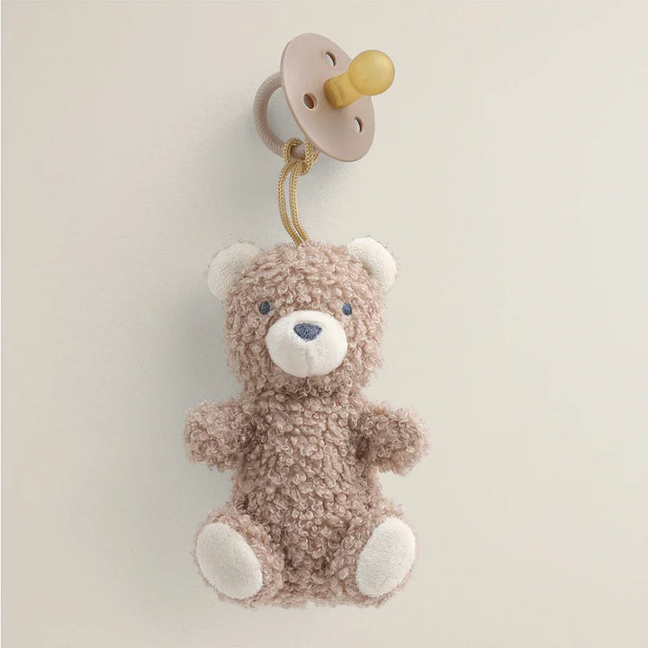 Natural rubber pacifier with plush teddy bear attachment against a neutral background
