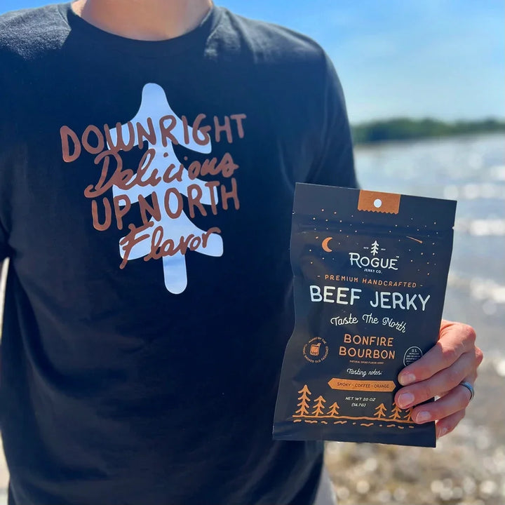 Person holding artisan beef jerky pouch labeled Bonfire Bourbon outdoors by water