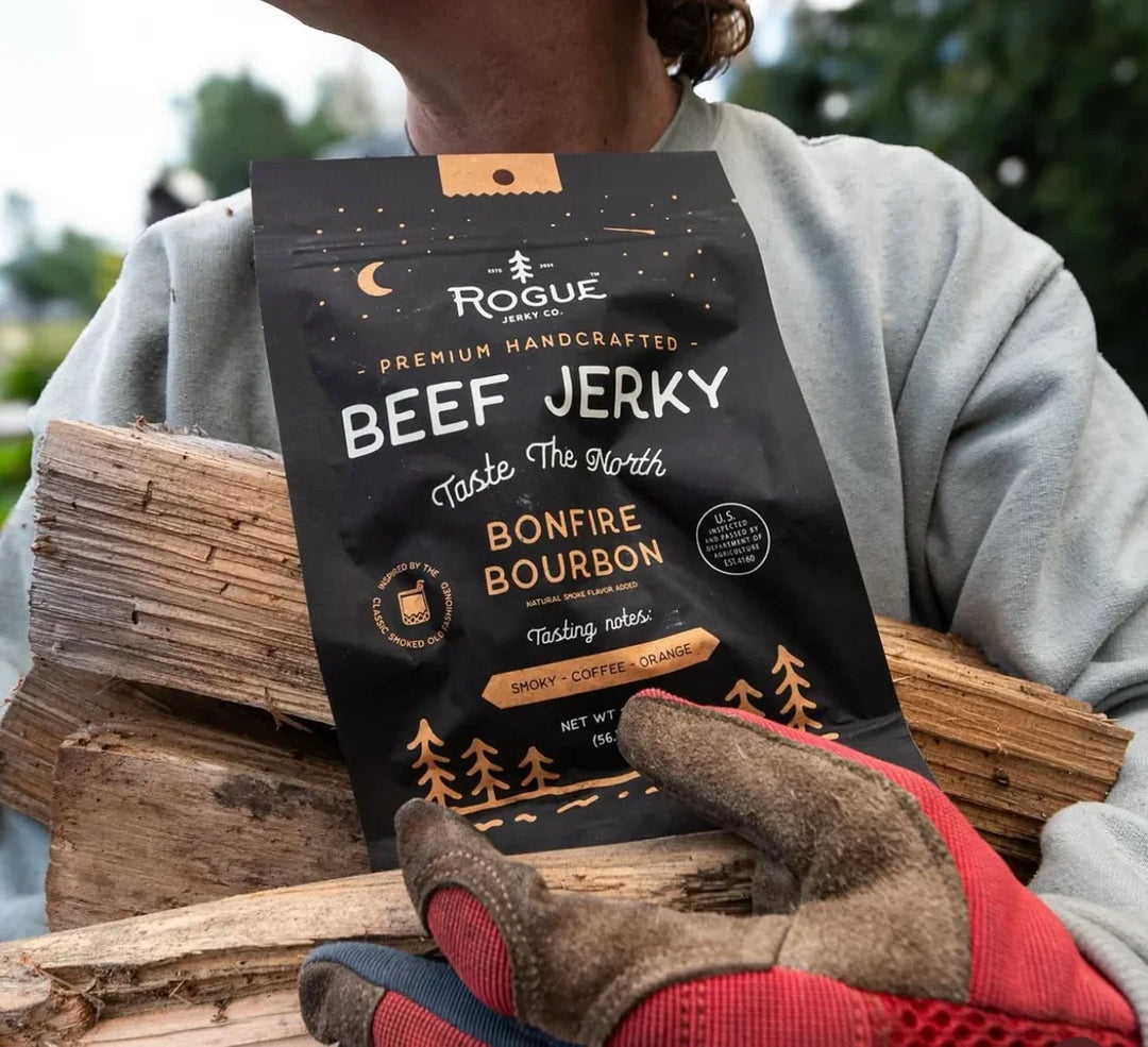 Bonfire Bourbon beef jerky pack held outdoors with firewood and work gloves