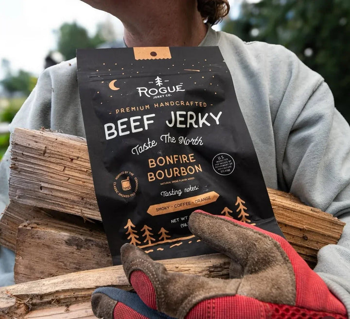 Bonfire Bourbon beef jerky pack held outdoors with firewood and work gloves