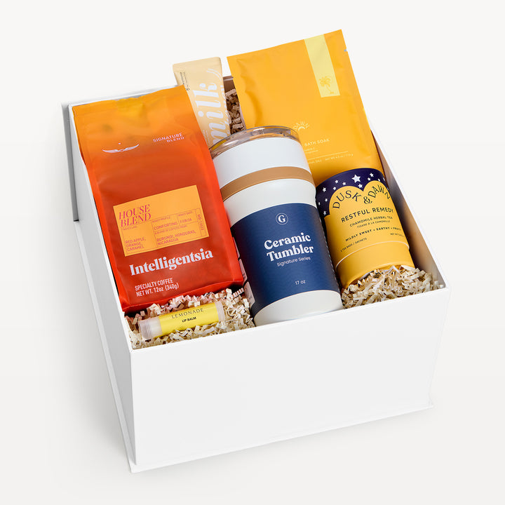 Bright Days Ahead Classic, white gift box, lid off. Intelligentsia House Blend coffee, navy Ceramic Tumbler, Restful Remedy tea, yellow Milk bar, orange and yellow packets. Giften Market.