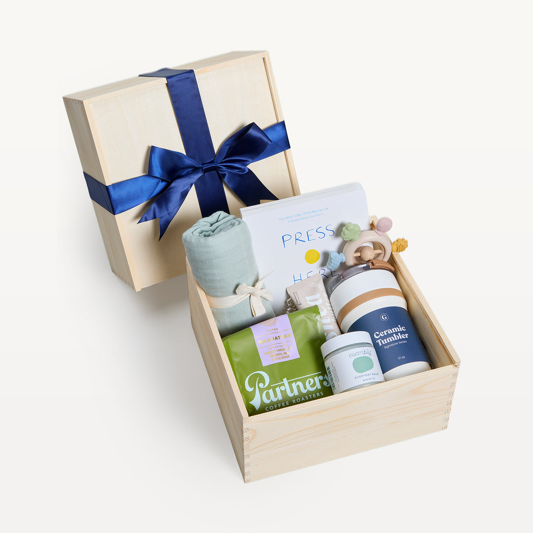 Bundle of Joy Sage Green crate open in front, bow-tied lid behind. Sage swaddle, Press Here book, Partners coffee, Ceramic Tumbler, everyday balm, wooden teether. Giften Market.