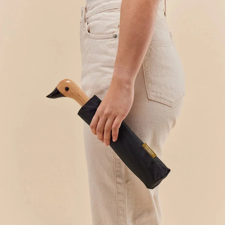 Person holding a folded black umbrella with a beige background