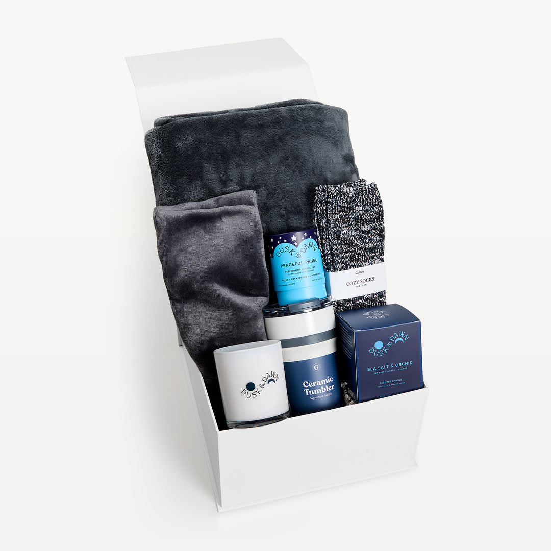 Comfort & Care for Men, white gift box, lid open. Charcoal faux-fur throw, marled Cozy Socks, Peaceful Pause tea, cream candle, Ceramic Tumbler, Sea Salt & Orchid candle box. Giften Market.
