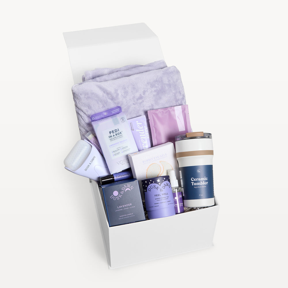 Comfort & Care Lavender, white gift box, lid open. Lilac faux-fur throw, Pedi in a Box, Bubbly Eye Gels, lavender packets, Dusk & Dawn Lavender candle, Feel Well tea, Ceramic Tumbler, spray. Giften Market.