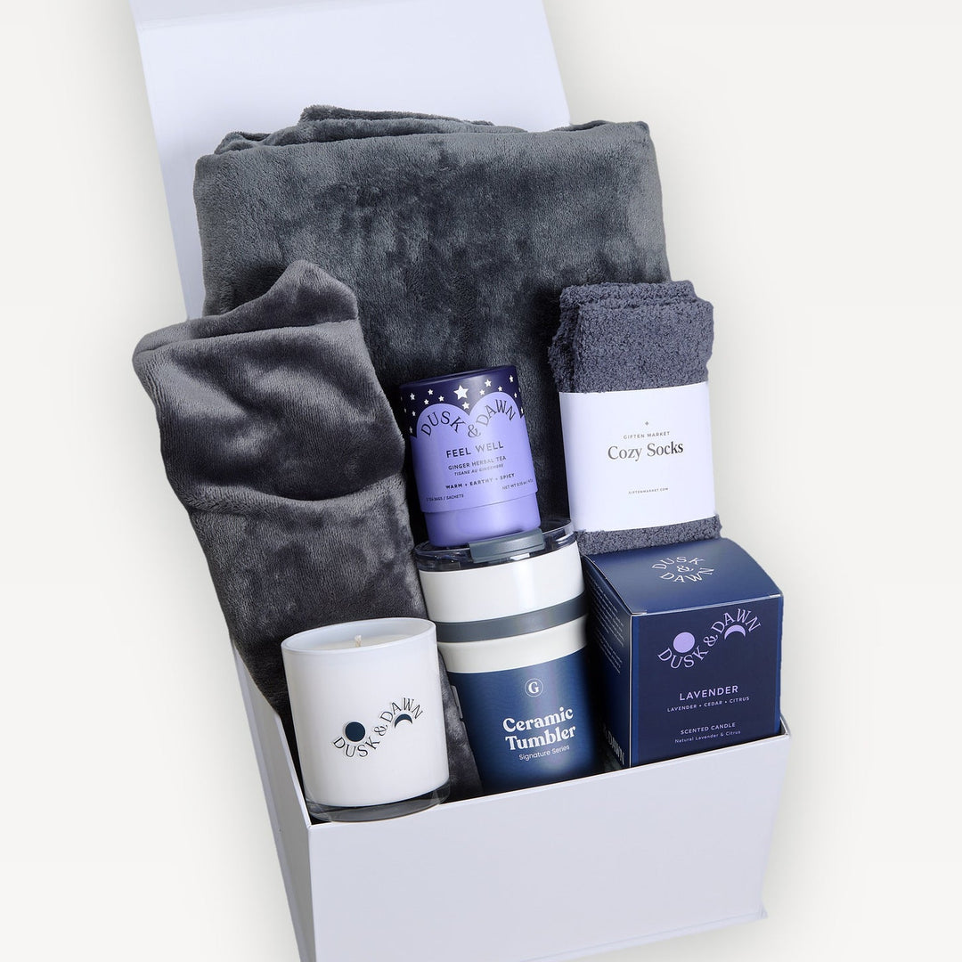 Comfort & Care Signature gift box in gray, lid open. Charcoal plush throw, gray heat-therapy neck wrap, Feel Well tin, Cozy Socks, Dusk & Dawn candle, Ceramic Tumbler, Lavender candle. Giften Market.