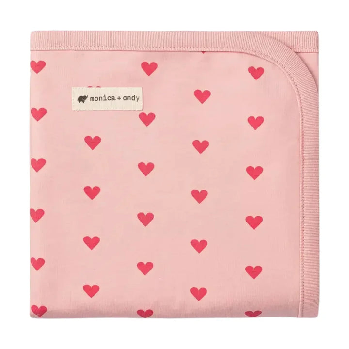 Pink baby blanket with red heart pattern, folded neatly, soft cotton fabric