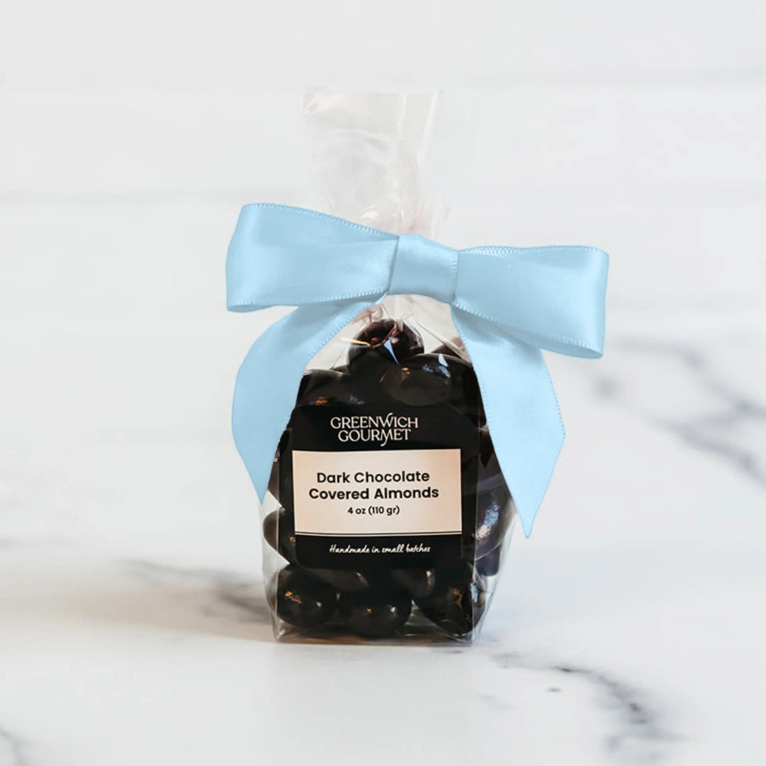 Dark chocolate covered almonds in a clear 4 oz bag tied with a light blue satin bow on a marble counter