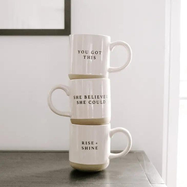 Stacked stoneware mugs with motivational phrases on a neutral table setting
