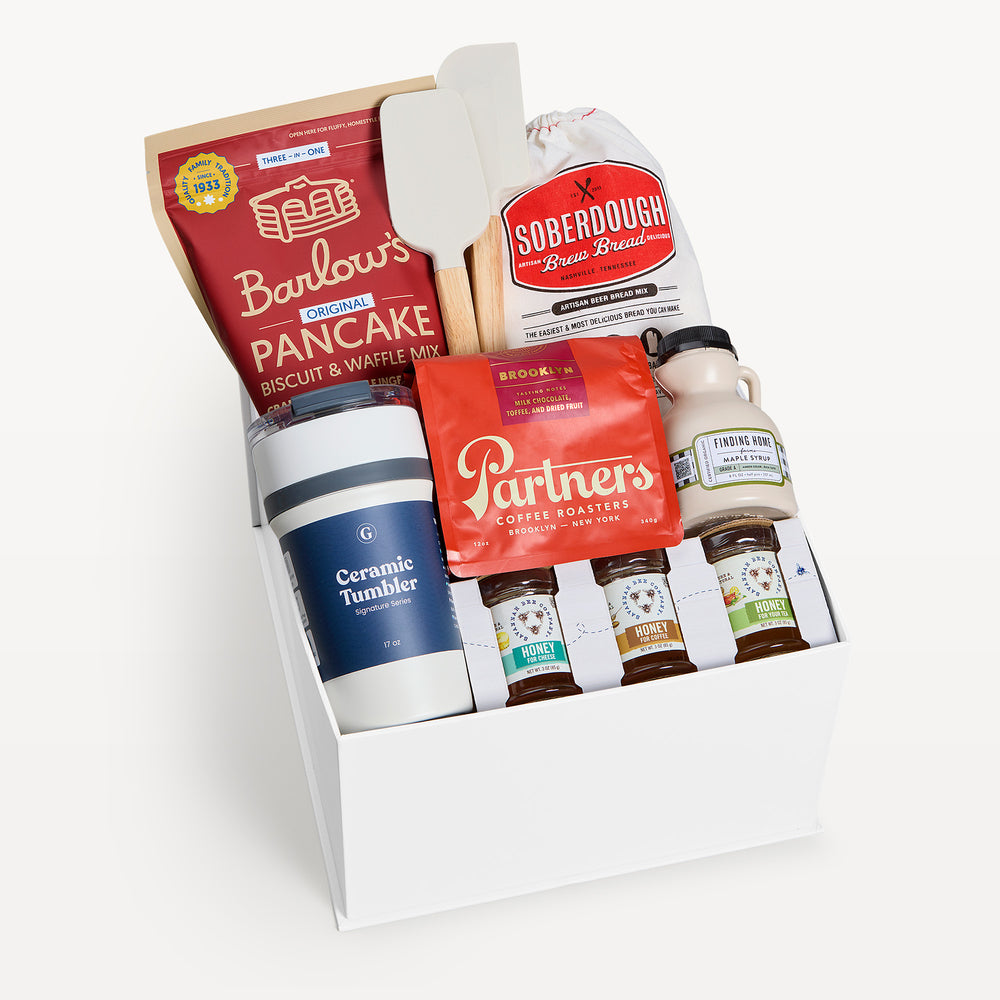 Good Morning Deluxe, white gift box, lid off. Barlow's pancake mix, Soberdough bread mix, wooden spatula, Partners coffee, maple syrup, three honey jars, navy Ceramic Tumbler. Giften Market.