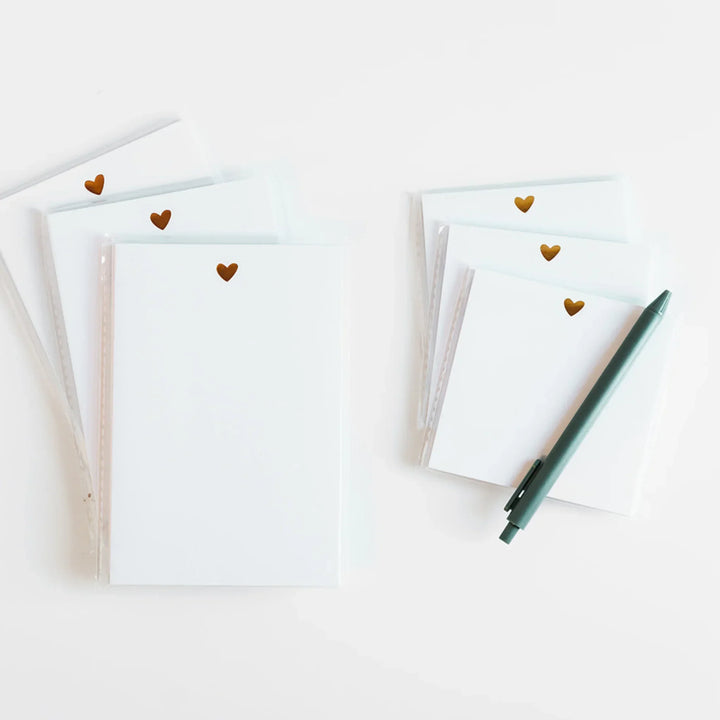 Stacks of white notepads with gold hearts and a green pen on a light background