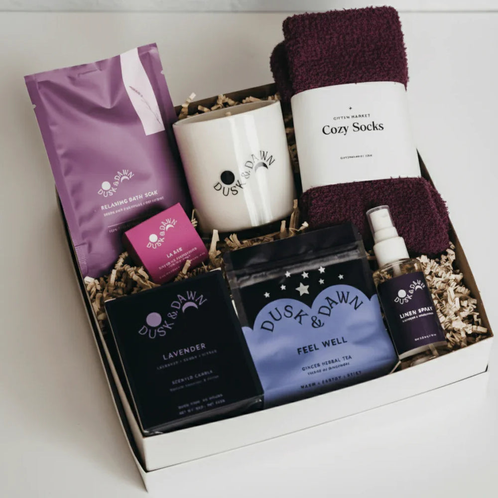 Lavender Luxuries Gift Box packed with plum cozy socks, lavender candle, relaxing bath soak, Feel Well tea and linen spray