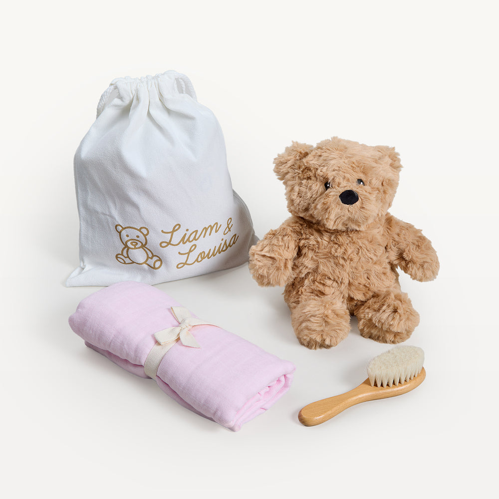 Liam & Louisa Snuggle Set, Archie Bear in pink, loose on the sweep: drawstring bag, tan bear, rolled pink swaddle, wooden brush. Giften Market.