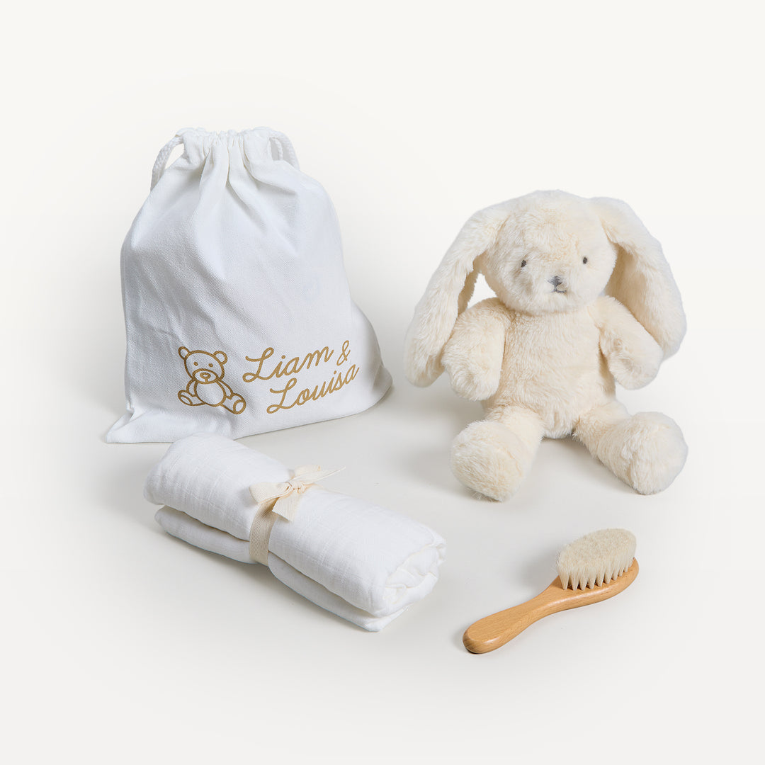 Liam & Louisa Snuggle Set, Bea Bunny in ivory, loose on the sweep: drawstring bag, cream bunny, rolled ivory swaddle, wooden brush. Giften Market.