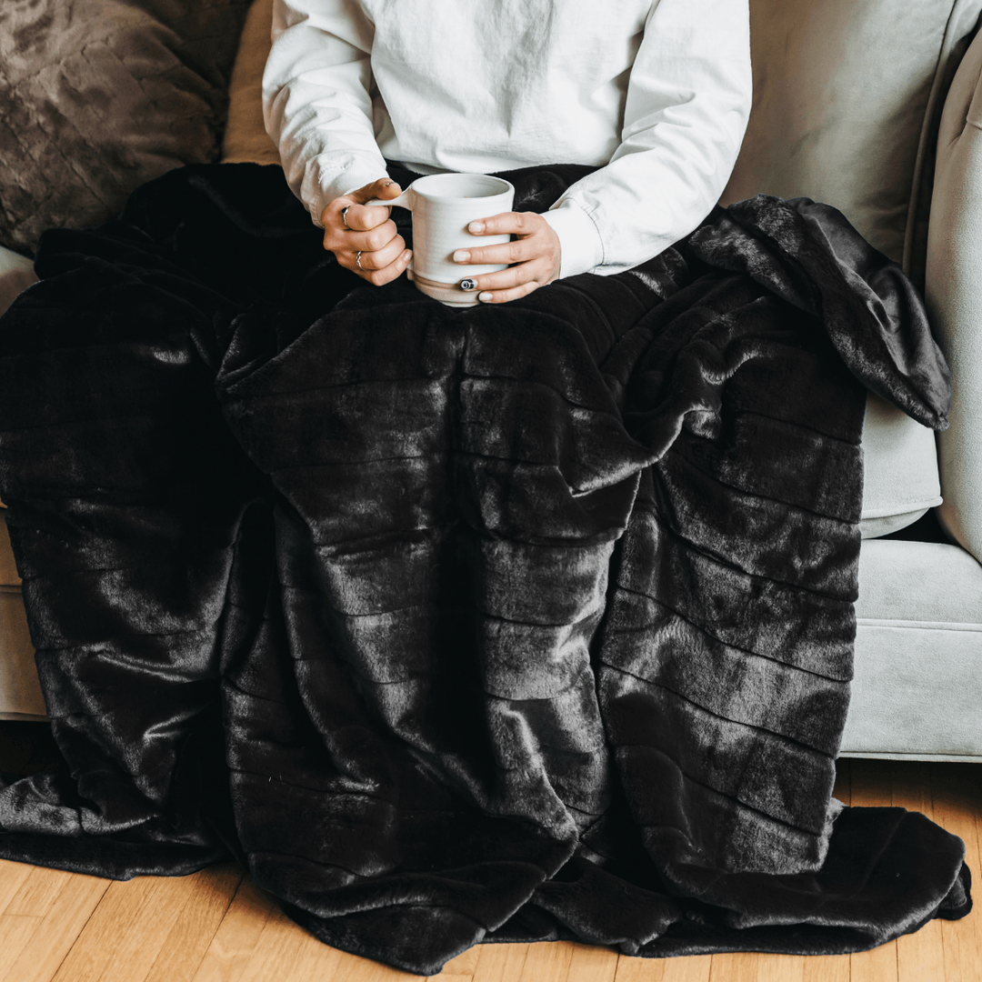 Person on a sofa under the black Luxe Faux Fur Throw Blanket holding a mug