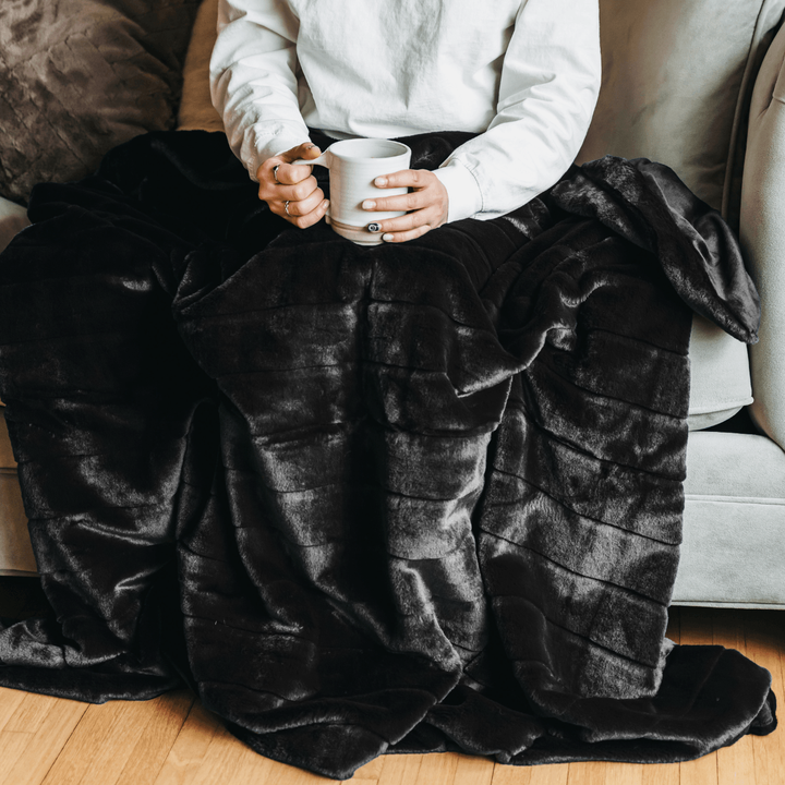 Person on a sofa under the black Luxe Faux Fur Throw Blanket holding a mug