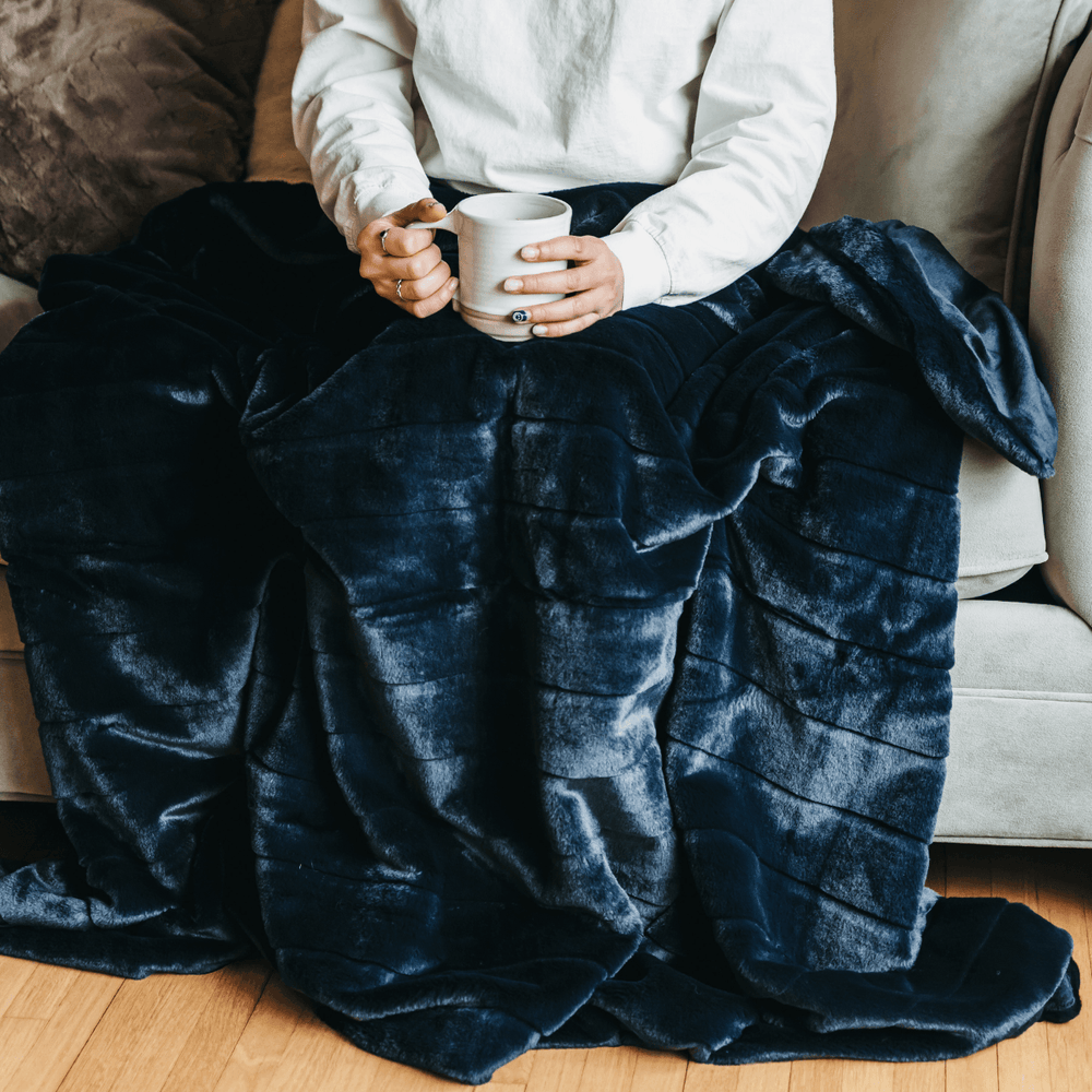 Person on a sofa under the navy Luxe Faux Fur Throw Blanket holding a mug