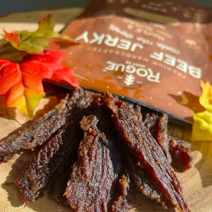 Sliced beef jerky on a wooden board with autumn leaves and branded snack packaging
