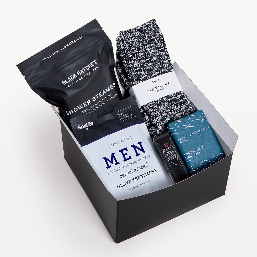 Men's Self-Care, black gift box, lid off. Black Hatchet shower steamer, marled Cozy Socks, SpaLife Men glacial mineral glove treatment, Oars + Alps, Epsom salt bar soap. Giften Market.