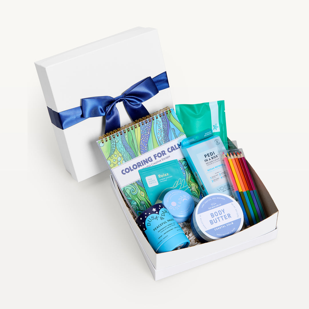 Mindfulness Classic, white shallow box open in front, bow-tied lid behind. Coloring for Calm book, pencils, teal packets, Pedi in a Box, Peaceful Pause tea, Coastal Calm body butter. Giften Market.