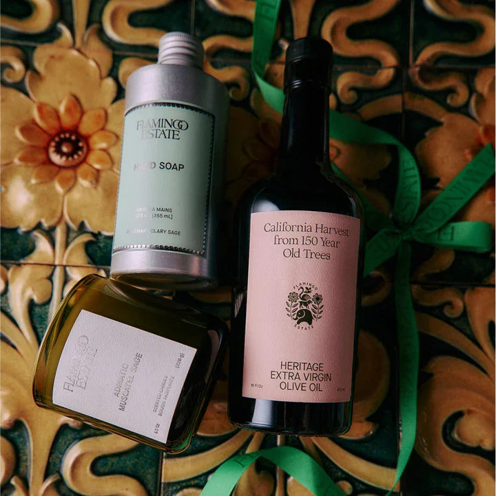 Gift set with olive oil, hand soap, and a candle on patterned tile with a green ribbon