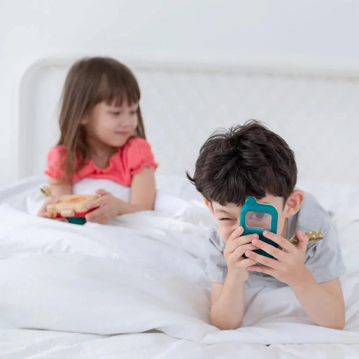 Children playing with wooden pretend phone and toy in bed, premium kids’ gift item