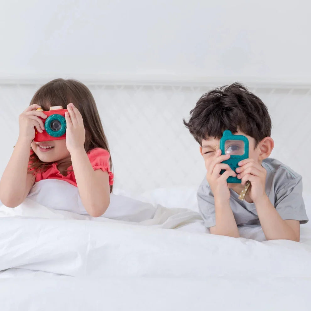 Two children on a bed playing with colorful toy camera and phone, white bedding background