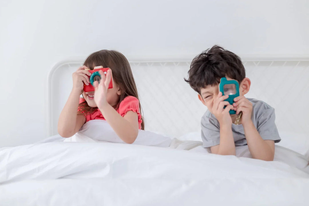 Two children in bed playing with colorful toy cameras, ideal for baby gift boxes