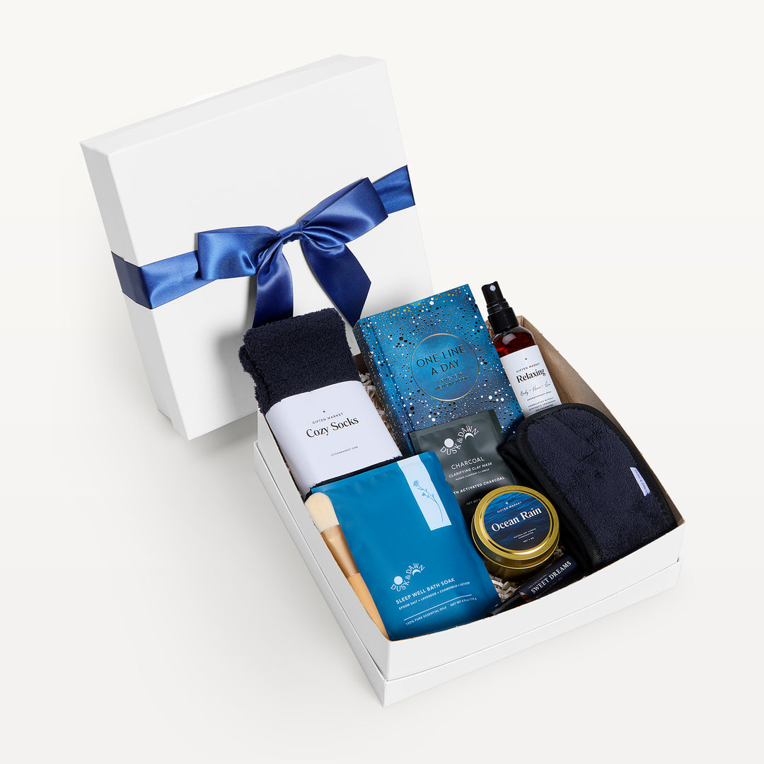Peaceful Retreat, white shallow box open in front, bow-tied lid behind. Black Cozy Socks, One Line a Day journal, Sleep Well bath soak, Ocean Rain tin, Relaxing spray, black eye mask, charcoal packet. Giften Market.