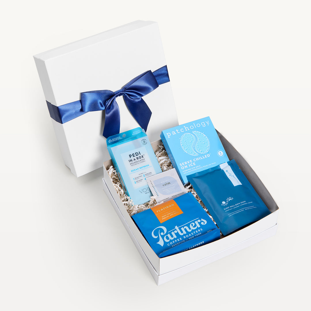 Relaxation Reset, white shallow box open in front, bow-tied lid behind. Patchology Serve Chilled eye gels, Pedi in a Box, Calm tin, Partners coffee, Sleep Well bath soak. Giften Market.